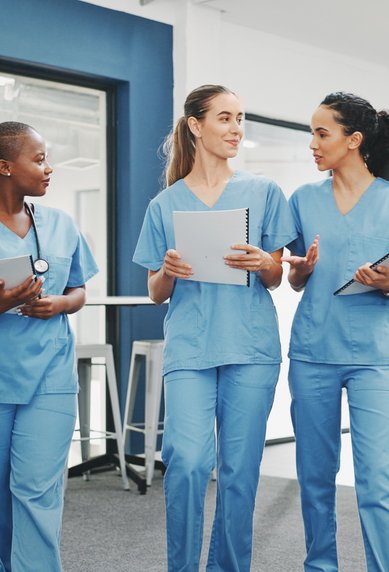 Drei medizinische Fachkräfte in blauen Scrubs gehen durch einen modernen Raum, während sie Tablets halten und miteinander sprechen.