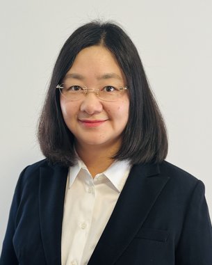 Eine Frau mit schulterlangen, glatten Haaren trägt einen schwarzen Blazer und ein weißes Hemd. Sie schaut direkt in die Kamera.