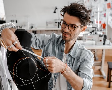 Ein Modedesigner misst mit einem Schneidermaßband an einer Schneiderpuppe in einem Atelier, um ein Kleidungsstück zu entwerfen.
