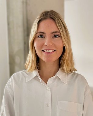 Young woman with shoulder-length blonde hair is wearing a white shirt and smiling warmly at the camera.