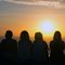 Six people are sitting side by side, watching the sunset on the horizon as the sky glows in warm colors.