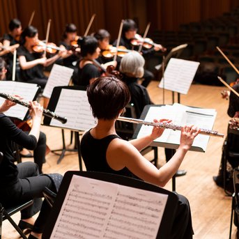 A orchestra with musicians playing various instruments, including flutes and violins, while a conductor leads.