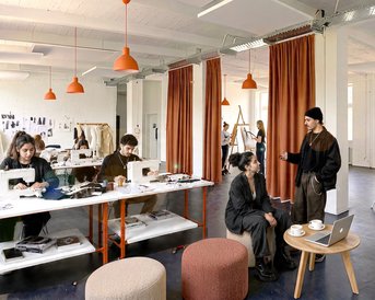 Ein kreativer Raum mit mehreren Arbeitsplätzen, an denen Menschen an Modeprojekten arbeiten. Einige Personen diskutieren, während andere konzentriert nähen oder entwerfen.