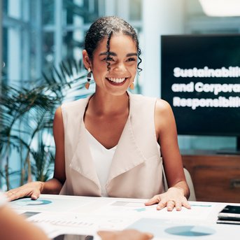 Zwei Frauen sitzen an einem Tisch und diskutieren. Im Hintergrund ist ein Bildschirm mit dem Text „Nachhaltigkeit und Unternehmensverantwortung“ zu sehen.