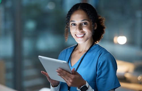 Eine Krankenschwester in blauer Uniform hält ein Tablet und lächelt, während sie in einem modernen, gut beleuchteten Raum steht.