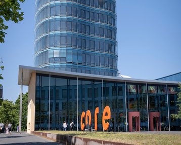 Hochhaus mit gläserner Fassade und abgerundetem Dach, im Vordergrund der Schriftzug "core" in orange.