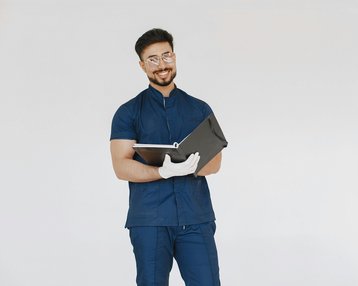 Ein lächelnder Mann in blauer Arbeitskleidung hält einen Ordner in der Hand. Er trägt eine Brille und weiße Handschuhe, während er vor einem neutralen Hintergrund steht.