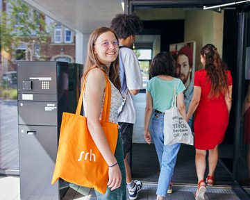 A group of four people enters a building. A woman with an orange bag smiles at the camera.