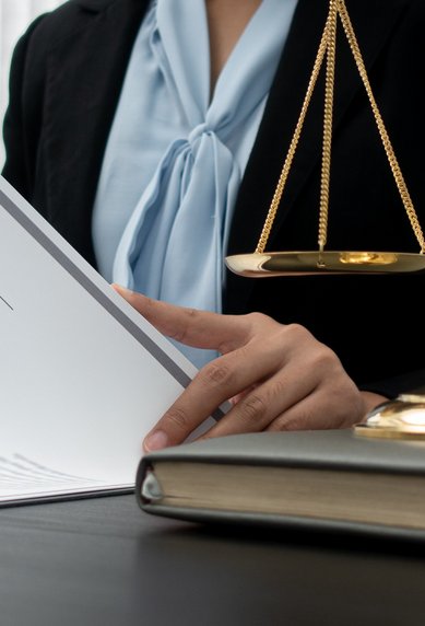 Eine Person in einem Anzug hält ein Dokument, während eine Waage und ein Richterhammer auf dem Tisch liegen.