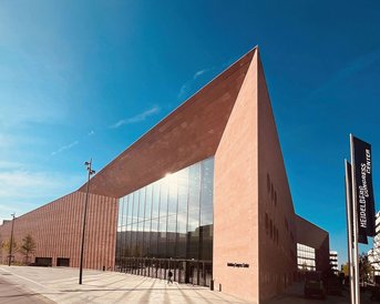 Modern architecture of the Heidelberg Congress Center featuring a striking slanted facade and large glass surfaces under a blue sky.