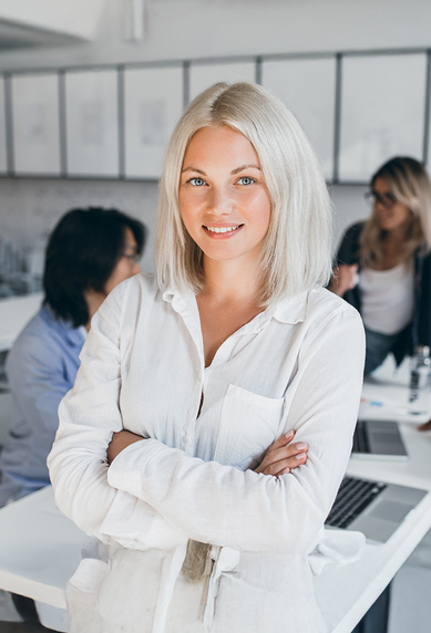A blonde woman is smiling in a modern office while three people are working at a table.