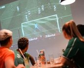 Eine Gruppe von Personen schaut auf eine große Leinwand, auf der ein Fußballspiel mit einem Elfmeter angezeigt wird.
