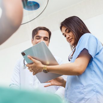 Zwei medizinische Fachkräfte besprechen Informationen auf einem Tablet in einem Behandlungsraum.