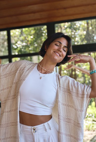 Eine Frau tanzt in einem hellen Raum mit großen Fenstern, während eine andere Frau im Hintergrund ebenfalls tanzt. Beide tragen lockere, helle Kleidung.