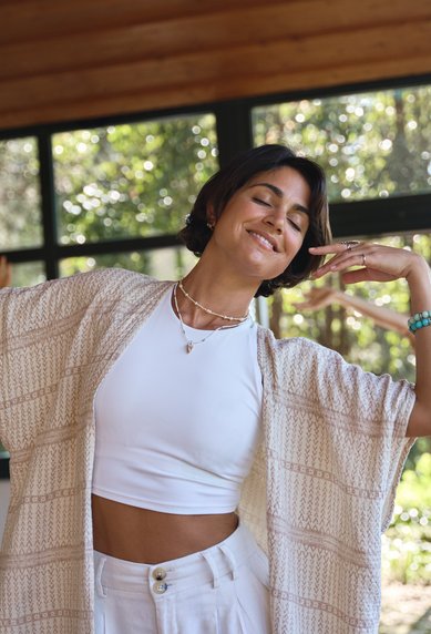 A woman dances in a bright room with large windows, while another woman dances in the background as well. Both are wearing loose, light-colored clothing.
