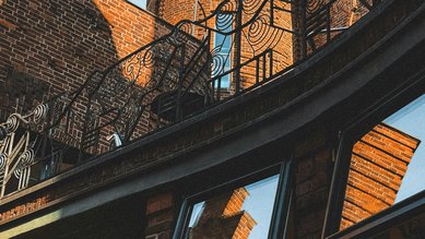 Turm mit kupferner Kuppel über Backsteinarchitektur, umgeben von geschwungenem Geländer und Fenstern, im klaren Himmel.