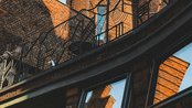 Turm mit kupferner Kuppel über Backsteinarchitektur, umgeben von geschwungenem Geländer und Fenstern, im klaren Himmel.