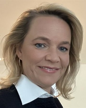 Eine Frau mit blonden Haaren und einem lächelnden Gesicht, trägt ein schwarzes Oberteil und ein weißes Hemd, posiert für ein Selfie.