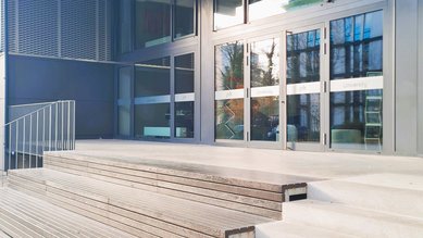 Eingang zum SRH Campus mit modernen Glastüren und Holzstufen. Der Schriftzug "Campus" ist über dem Eingang sichtbar.