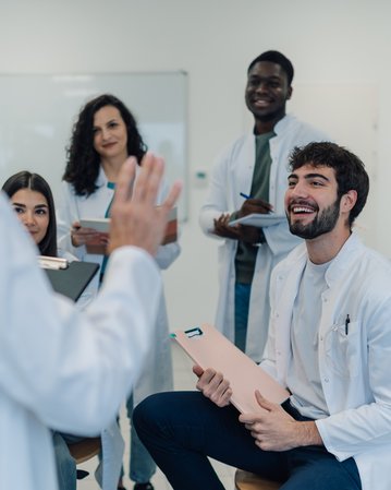 Eine Gruppe von fünf Personen in Laborkitteln, die in einem modernen Raum stehen und sich unterhalten. Ein Mann lächelt, während eine Frau spricht.
