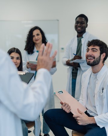 A group of five people in lab coats standing in a modern laboratory. One person is speaking while the others listen attentively.