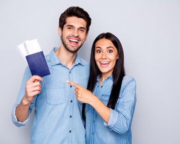 Ein Mann und eine Frau in blauen Hemden halten einen Reisepass und Tickets, lächeln und zeigen auf den Reisepass.