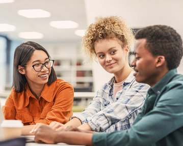 Studierende sitzen lachend am Tisch und arbeiten