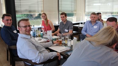 Eine Gruppe von sechs Personen sitzt an einem Tisch in einem Restaurant, lächelnd und mit Getränken vor sich.