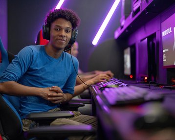 Ein junger Mann mit Kopfhörern sitzt an einem Computerarbeitsplatz in einem Gaming-Raum, bereit zum Spielen.