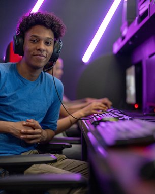 Ein junger Mann mit Kopfhörern sitzt an einem Computerarbeitsplatz in einem Gaming-Raum, bereit zum Spielen.