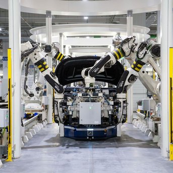 A modern assembly line with several industrial robots assembling a vehicle. The environment is brightly lit and showcases a state-of-the-art production facility.