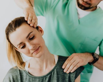 Kategorie Therapie studieren Studium SRH University Eine Frau erhält eine Nackenmassage von einem männlichen Therapeuten. Der Therapeut hat seine Hand auf ihren Kopf gelegt, während sie entspannt aussieht. Beide tragen bequeme Kleidung.