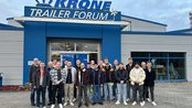 Gruppe von jungen Erwachsenen steht vor dem Krone Trailer Forum, lächelnd und in Freizeitkleidung, mit dem Gebäude im Hintergrund.