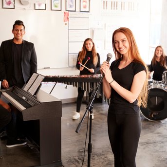A group of five musicians in black clothing playing instruments while a singer holds a microphone.