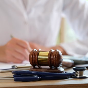 Ein Arzt mit einem Stethoskop und einem Richterhammer auf dem Tisch, während er Notizen macht.