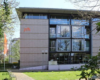 Moderne Gebäude mit großen Fenstern und dem Logo "srh" an der Fassade, umgeben von Bäumen und einem grünen Bereich.