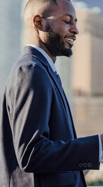 A man in a suit stands on a bridge, looking at his smartphone while surrounded by modern buildings.