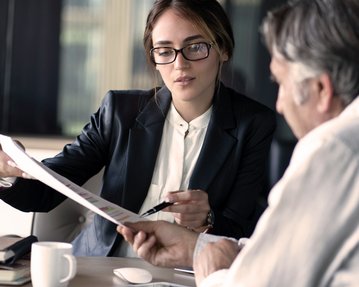 A woman in a suit is showing a man a document during a conversation in a modern office.