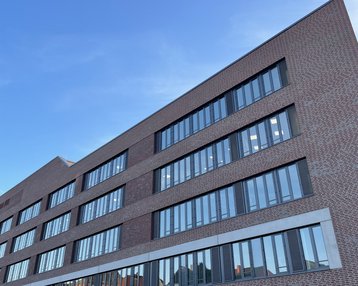 Moderne Backsteinfassade eines Gebäudes mit großen Fenstern und klaren Linien, unter einem blauen Himmel.