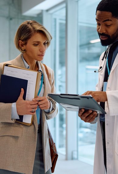 A doctor in a white coat is showing a woman and a nurse information on a tablet in a modern hospital setting.