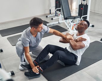 Ein Trainer unterstützt einen Mann bei einer Übung im Fitnessstudio, während er ihm hilft, die richtige Technik zu verwenden.