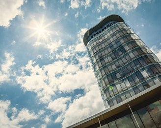 Ein modernes Hochhaus mit einer geschwungenen Fassade, das unter einem klaren Himmel mit Wolken und Sonnenschein steht.