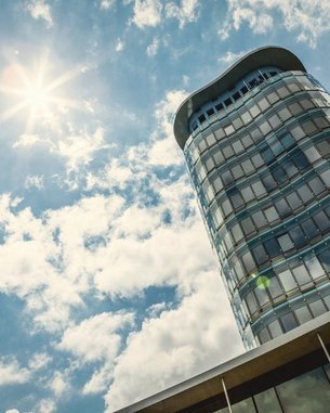 A modern high-rise building with a curved facade, standing under a clear sky with clouds and sunshine.