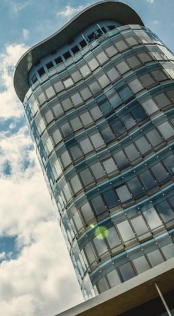 Ein modernes Hochhaus mit einer geschwungenen Fassade, das unter einem klaren Himmel mit Wolken und Sonnenschein steht.