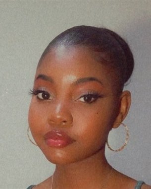 Eine junge Frau mit kurzem, glattem Haar und großen Ohrringen schaut direkt in die Kamera. Sie trägt einen dezenten, natürlichen Make-up-Look.