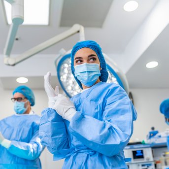 Ein Team von Chirurgen in blauen OP-Kitteln und Masken bereitet sich in einem Operationssaal auf einen Eingriff vor.