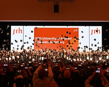 Graduates of the SRH University of Applied Sciences celebrate their graduation as they toss their caps into the air.