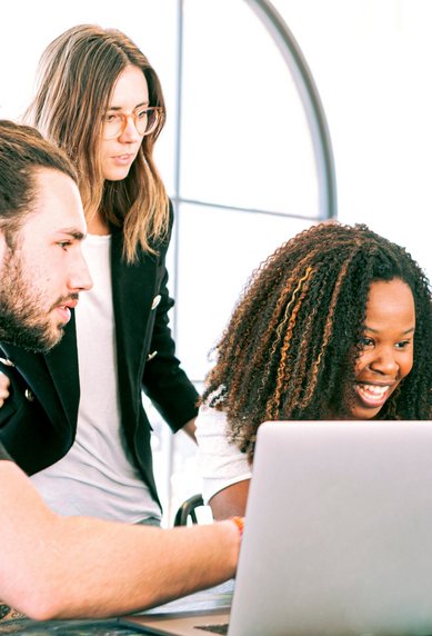 Eine Gruppe von vier Personen schaut auf zwei Laptops und lächelt, während sie zusammenarbeiten. Die Atmosphäre ist freundlich und kooperativ.