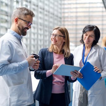 Drei medizinische Fachkräfte unterhalten sich in einem modernen Krankenhausumfeld, während eine weitere Person im Hintergrund steht.
