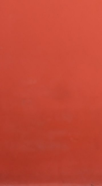 Eine Frau mit Zopf trägt einen orangefarbenen Hoodie und schwarze Hosen, während sie an einer roten Wand entlanggeht und auf ihr Handy schaut.